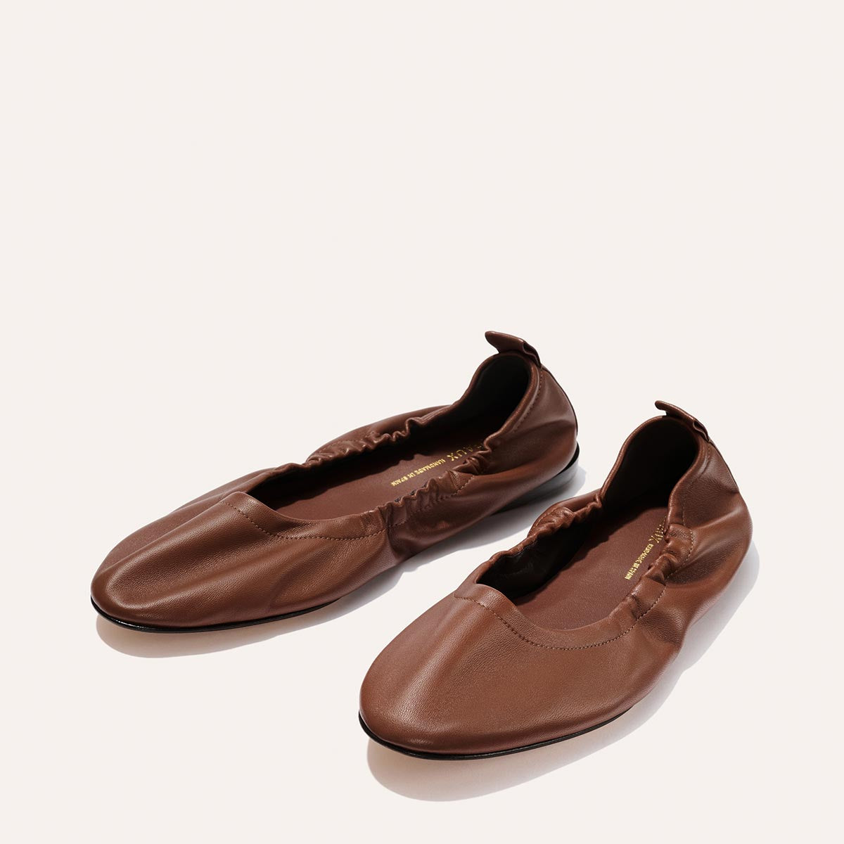 The Pascale - Cognac Nappa by Margaux: brown leather ballet flats with gathered elastic sides and rounded toes, shown on a light background.