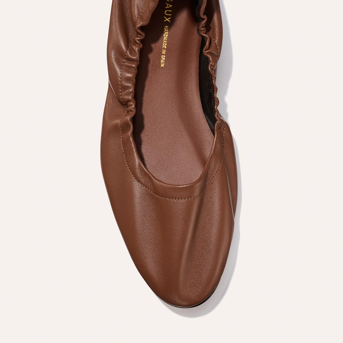 A close-up of The Pascale - Cognac Nappa by Margaux, a brown ballet flat featuring a gathered elastic edge and smooth leather texture, shown on a plain white background.