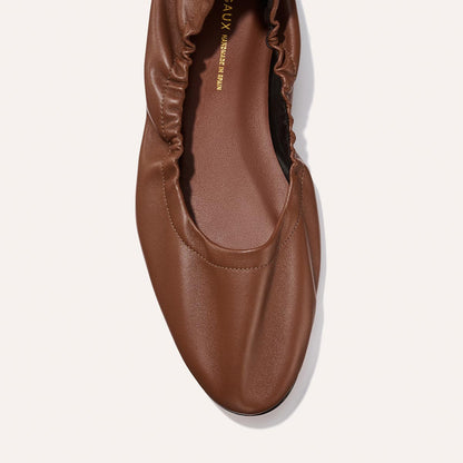 A close-up of The Pascale - Cognac Nappa by Margaux, a brown ballet flat featuring a gathered elastic edge and smooth leather texture, shown on a plain white background.