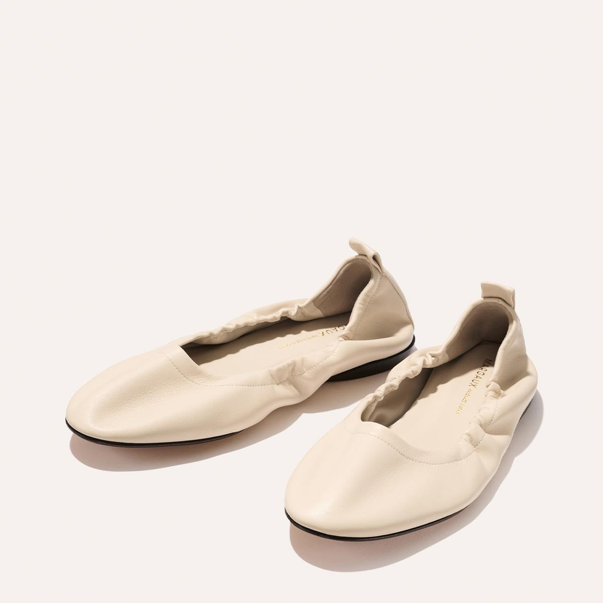 The Pascale - Bone Nappa by Margaux: cream-colored ballet flats with ruched edges and a back pull tab, set against a plain, light background.