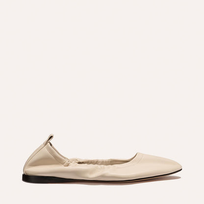 Side view of Margaux’s The Pascale - Bone Nappa: a cream ballet flat with a pointed toe, elasticized opening, small heel pull tab, and flat black sole, displayed on a plain light background.
