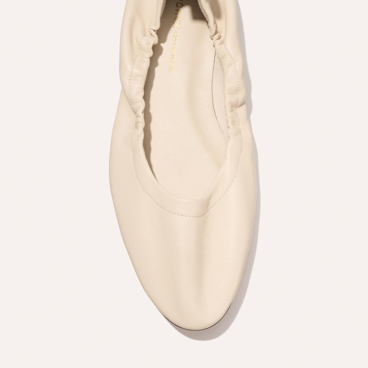 A top view of The Pascale - Bone Nappa by Margaux, a cream-colored flat shoe featuring a rounded toe and ruched detailing around the opening, photographed on a plain light background.