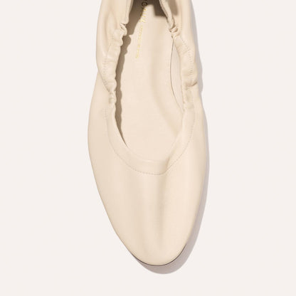 A top view of The Pascale - Bone Nappa by Margaux, a cream-colored flat shoe featuring a rounded toe and ruched detailing around the opening, photographed on a plain light background.