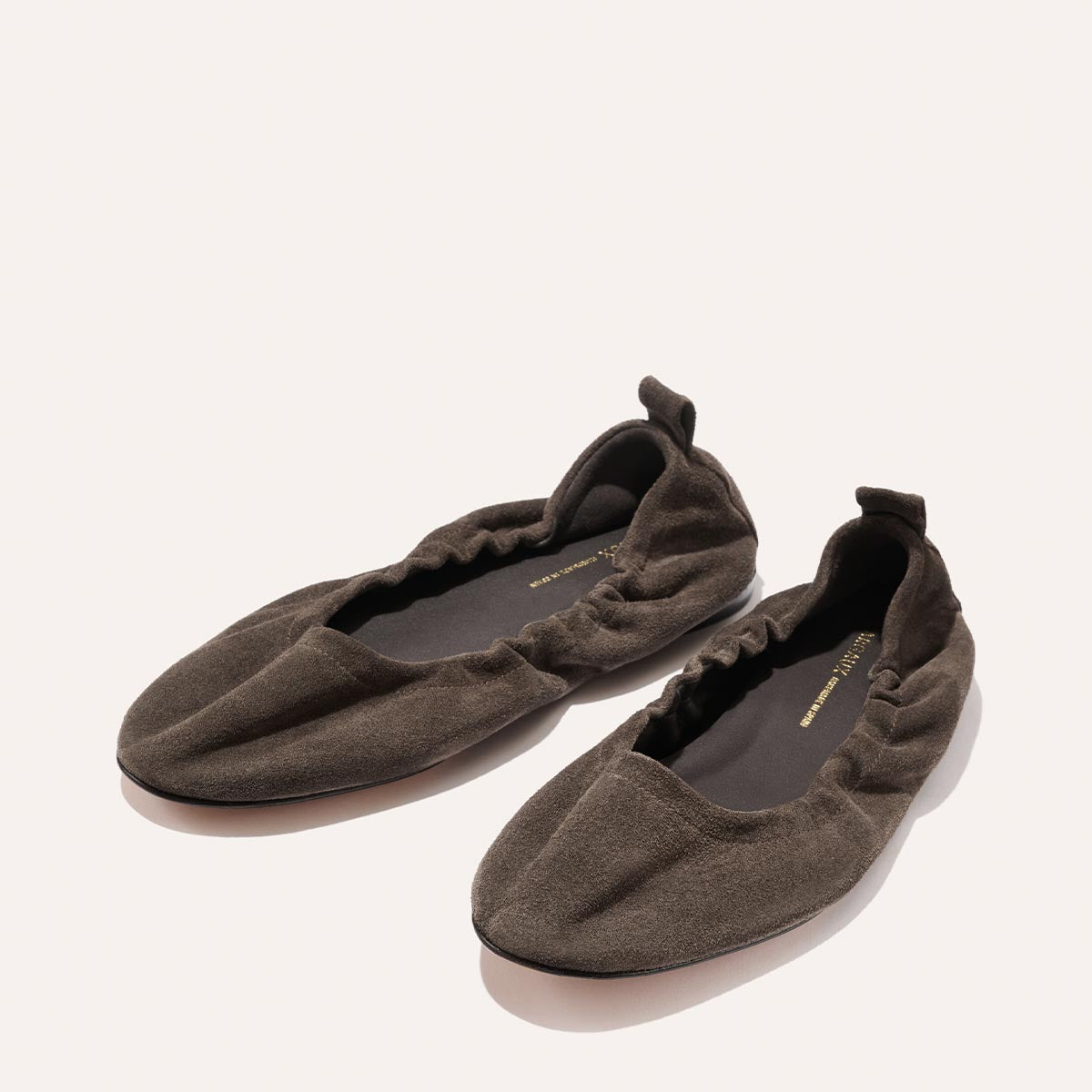 A pair of The Pascale ballet flats by Margaux in English Brown suede, featuring ruched detailing and an elasticated back, crafted from supple leather and showcased on a neutral background.