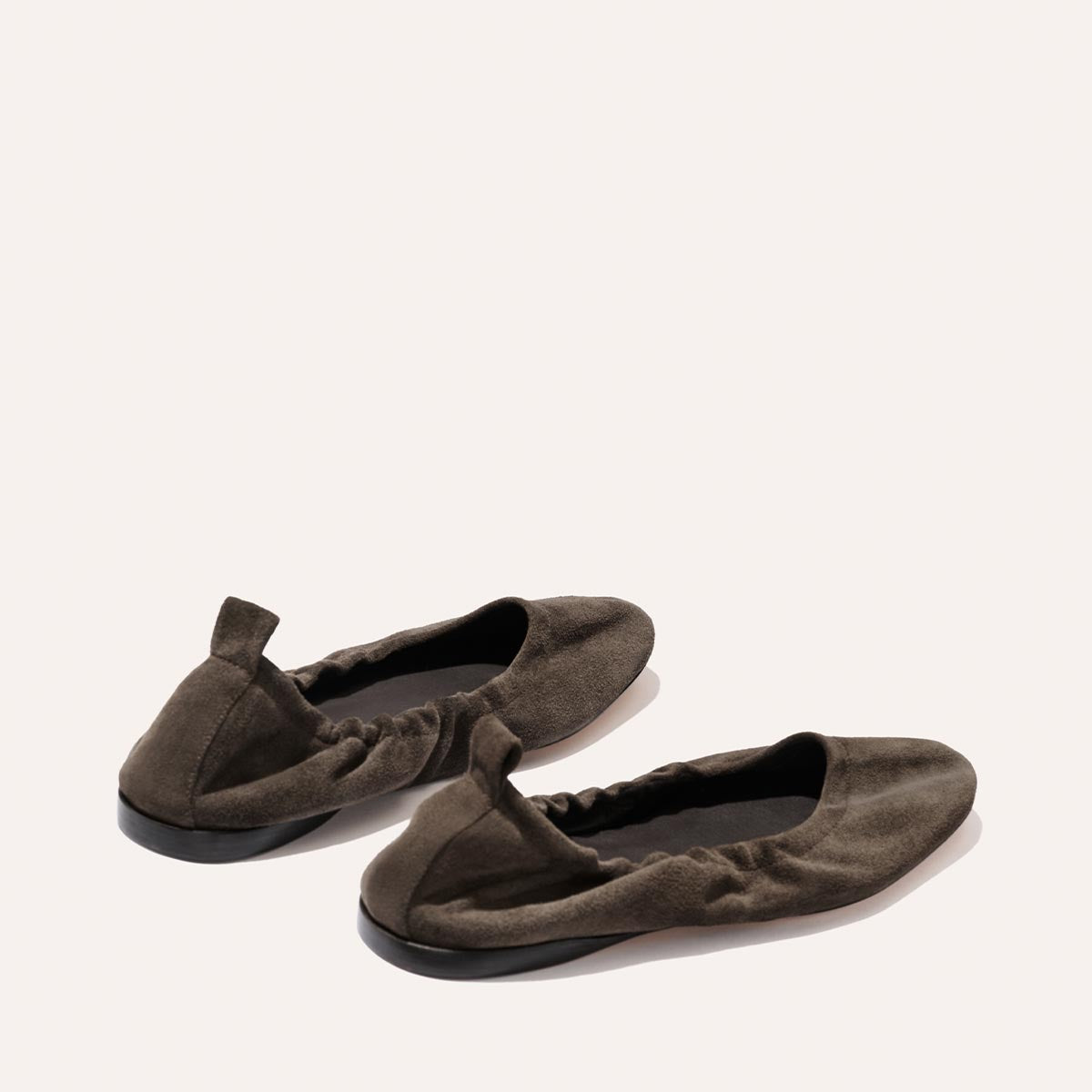 A pair of The Pascale - English Brown Suede ballet flats by Margaux, featuring supple dark brown suede, an elasticated back, and black soles, elegantly displayed on a light background.