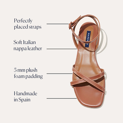 The Flat Sandal - Saddle Nappa by Margaux features a minimalist brown design with ankle and crisscross straps. Handmade in Spain from soft Italian nappa leather, it includes 5mm plush foam padding for comfort.