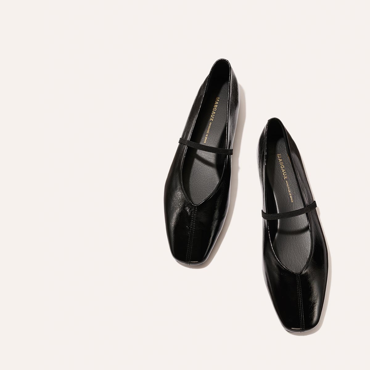 The Phoebe - Black Crinkle-Gloss Nappa by margaux-development: black leather ballet flats with sacchetto construction and a slim top strap, shown on a light beige background.