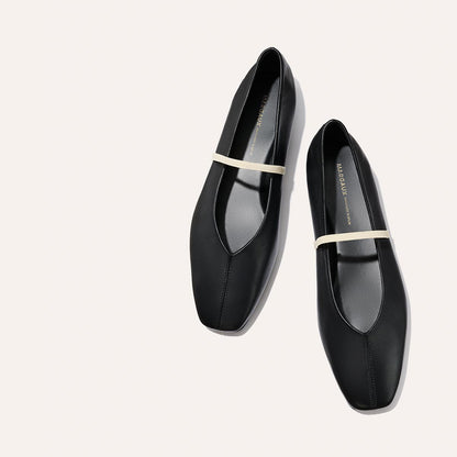 The Phoebe - Black and Ivory Nappa by margaux-development: black leather ballet flats with a square toe, thin ivory strap, and sacchetto construction for comfort, shown on a light beige background.