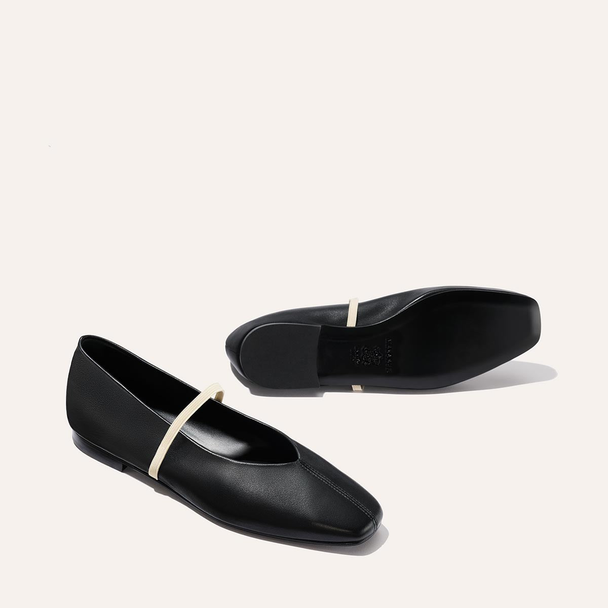 The Phoebe - Black and Ivory Nappa flats by margaux-development feature deconstructed black leather, square toes, and thin light beige straps. Displayed on a light background—one upright, the other lying on its side.
