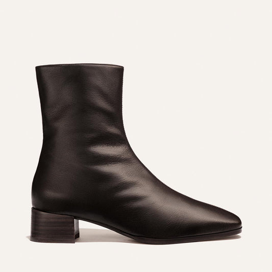 A dark chocolate calf leather ankle boot by Margaux, The Phoebe Boot features a mid-low stacked leather heel, rounded toe, and smooth finish. Shown in profile against a plain light background, this timeless style exudes understated elegance and modern design.