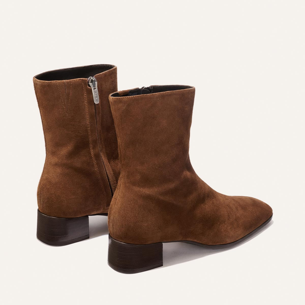 The Phoebe Boot - Ganache Suede by Margaux features brown suede ankle boots with side zippers and low, dark wooden heels, expertly crafted using the artisanal sacchetto technique for superior flexibility and comfort, shown against a plain light background.