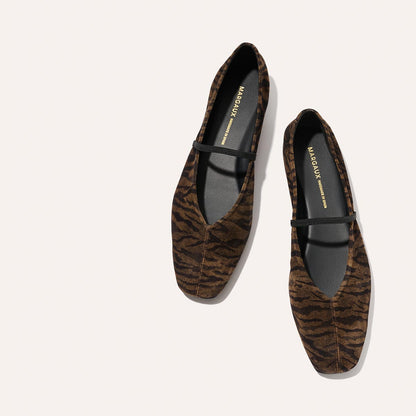 Margaux’s The Phoebe - Brown Zebra Suede flats feature a brown and black zebra stripe pattern, black interior, and a thin black strap across the top, shown on a light background.