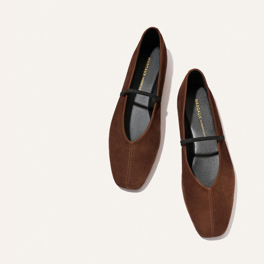 A pair of The Phoebe - Ganache Suede Mary Jane flats by Margaux, featuring brown suede uppers, thin black straps, and black insoles. Crafted with sacchetto construction for exceptional softness, they are shown on a plain white background.
