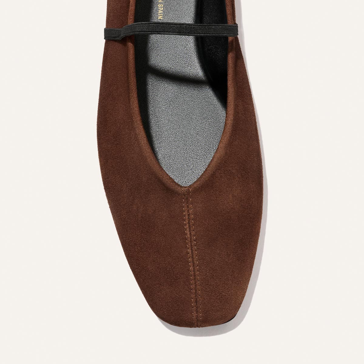 A close-up of The Phoebe - Ganache Suede flat by Margaux, featuring a brown suede deconstructed design with a square toe and a thin black strap across the top, shown against a light background.