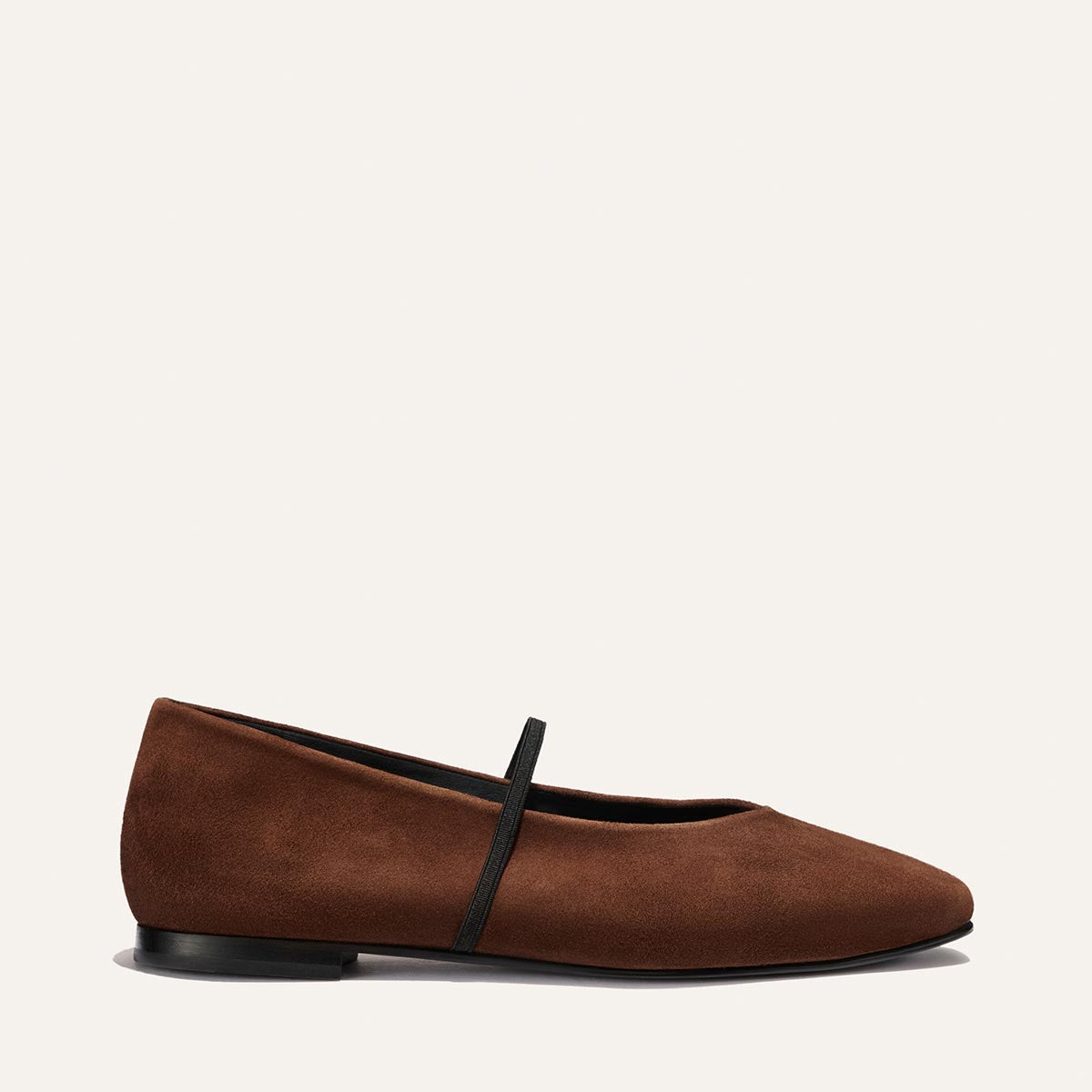 The Phoebe - Ganache Suede by Margaux is a brown suede ballet flat with a black sole and a single thin black strap across the top, shown in profile against a plain light background. This deconstructed flat features sacchetto construction for exceptional comfort and flexibility.