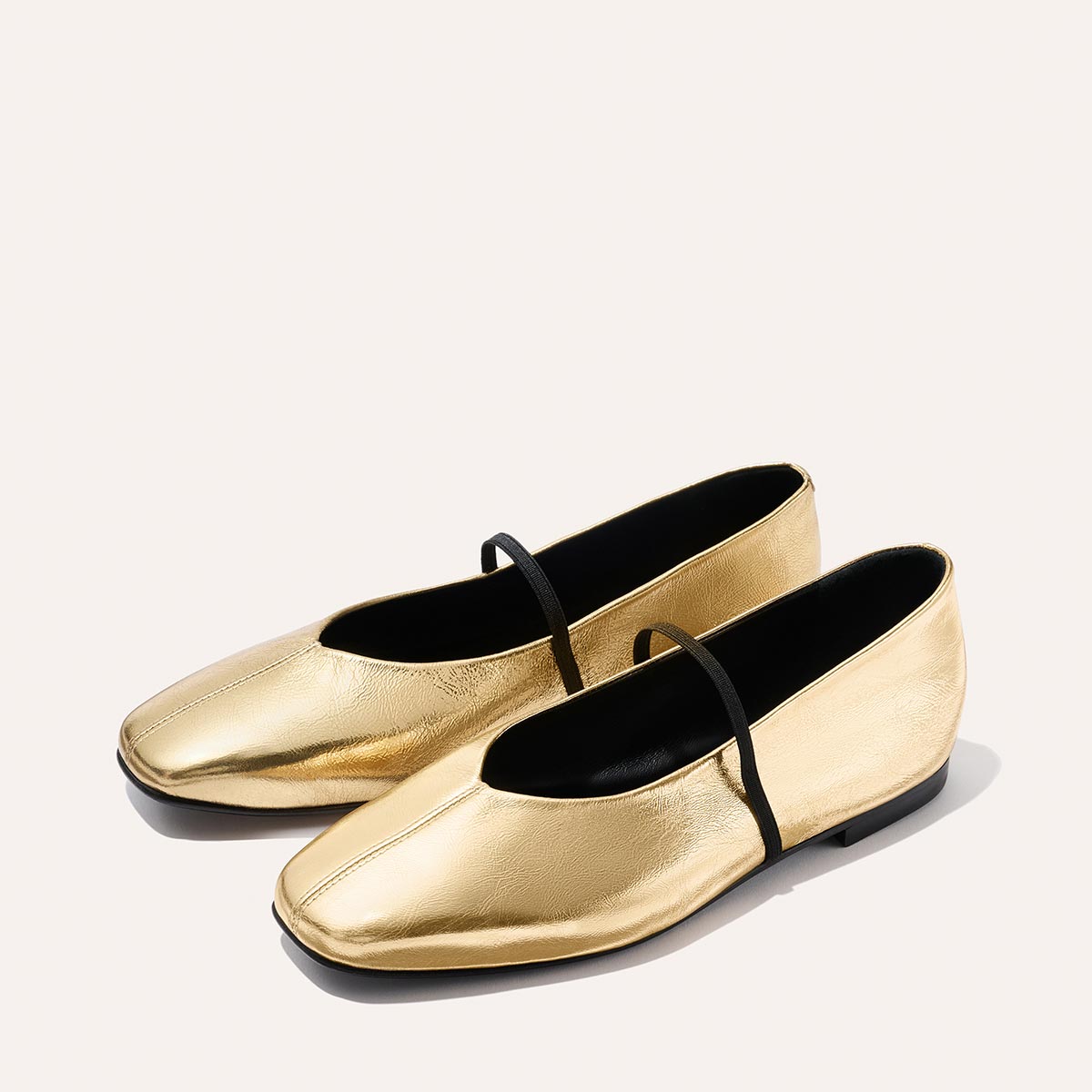 The Phoebe - Gold Crinkle Nappa by margaux-development: shiny gold square-toe ballet flats with a thin black strap and sacchetto construction for extra softness, shown on a light background.