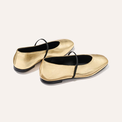 The Phoebe - Gold Crinkle Nappa by margaux-development: shiny gold ballet flats with black soles and a single thin black strap, crafted in sacchetto construction for a soft, comfortable fit, displayed on a light background.
