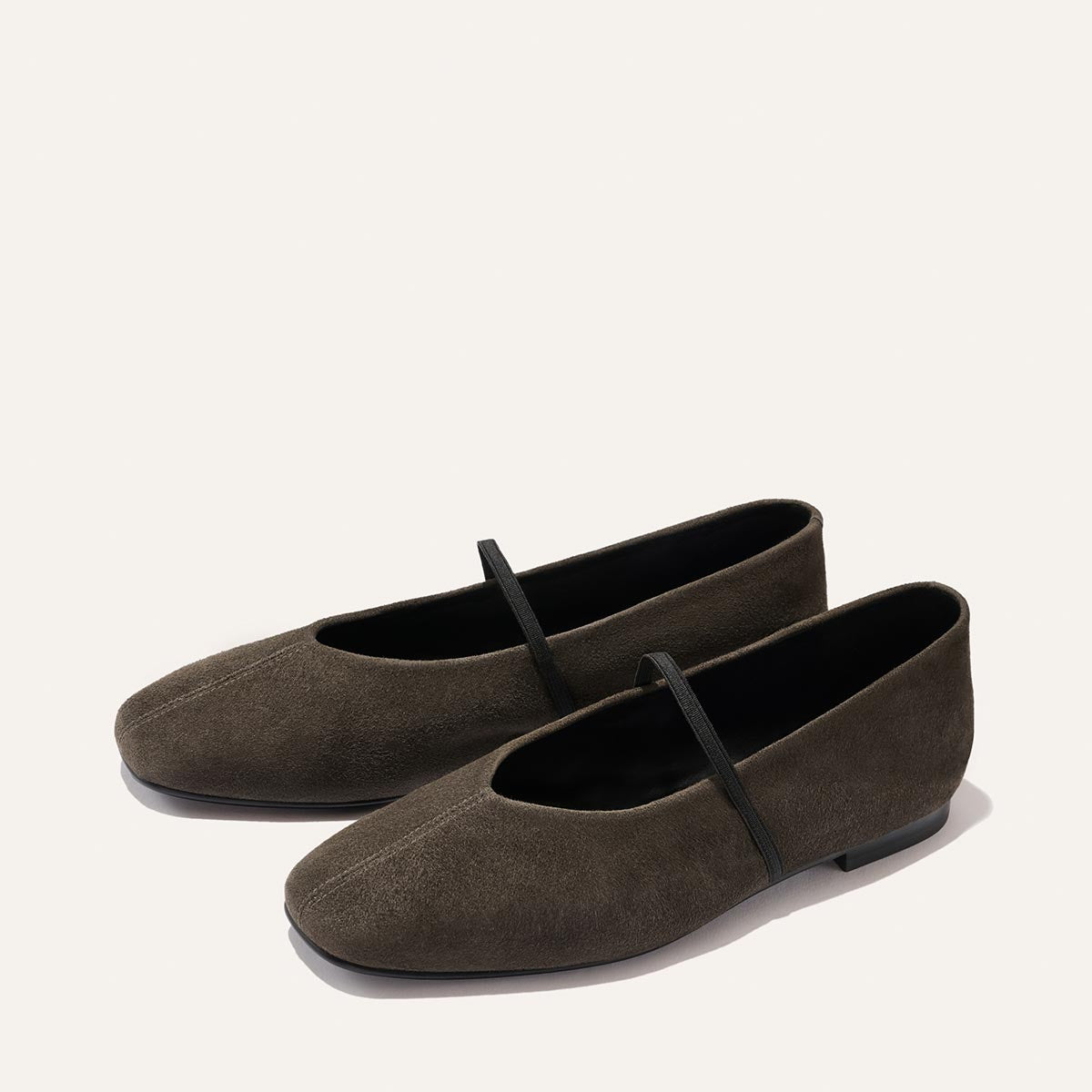 A pair of The Phoebe ballet flats in graphite suede by Margaux, featuring black straps over the top and shown on a light background. Expertly handmade using sacchetto construction, these shoes promise exceptional comfort and elegance.