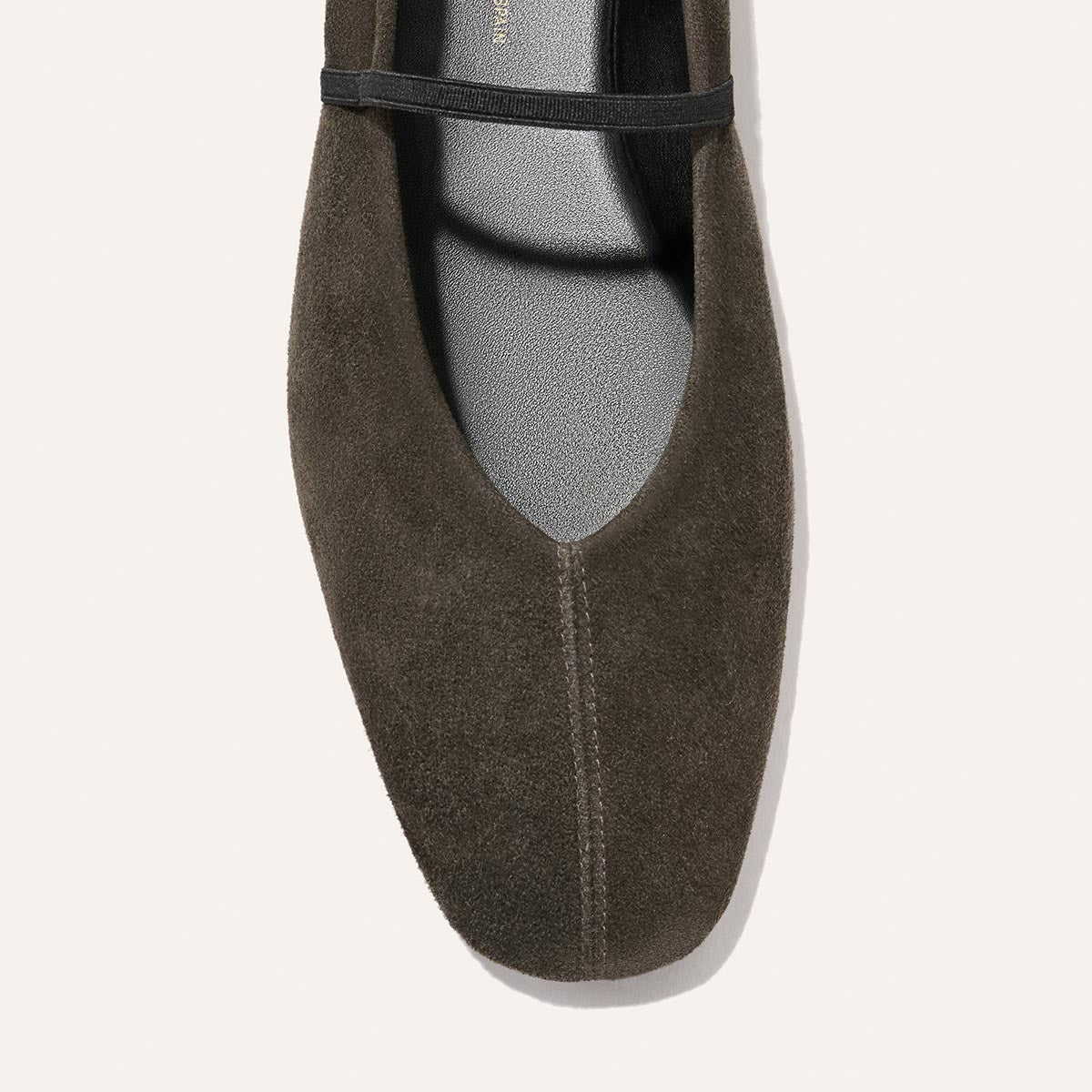 A top view of Margaux’s The Phoebe in Graphite Suede, a single dark brown suede flat featuring a black elastic strap, stitched center seam, and sacchetto construction for exceptional handmade comfort.