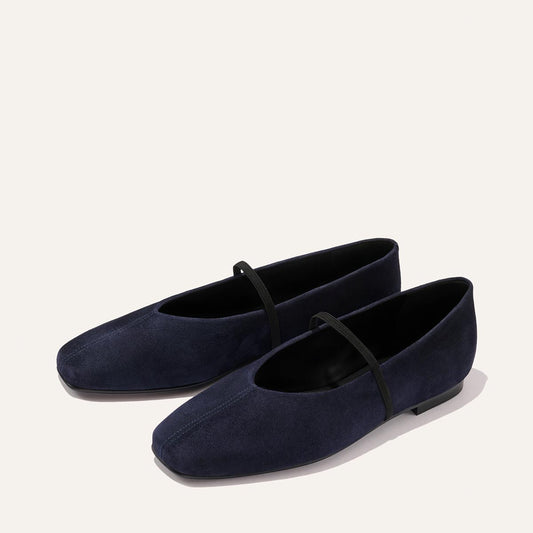 A pair of The Phoebe - Indigo Suede ballet flats by Margaux, featuring rich navy blue suede and a black strap across the top, expertly crafted with sacchetto construction for exceptional flexibility and comfort, displayed on a light background.