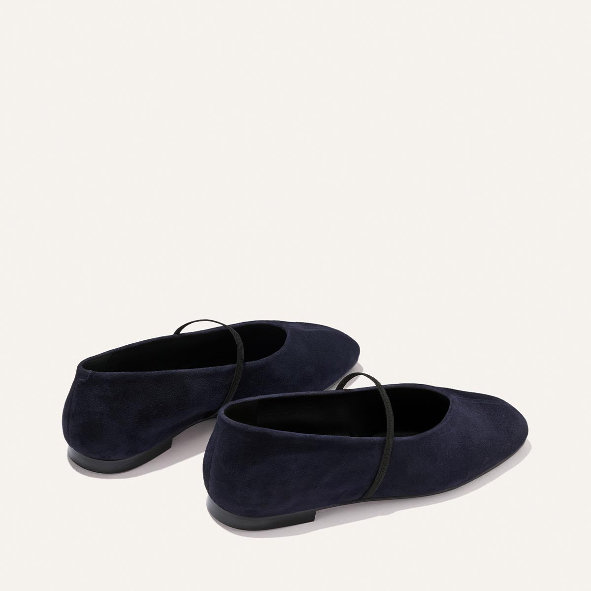 The Phoebe - Indigo Suede by Margaux is a pair of dark navy suede ballet flats featuring thin black straps and crafted with sacchetto construction for exceptional comfort, shown against an off-white background.