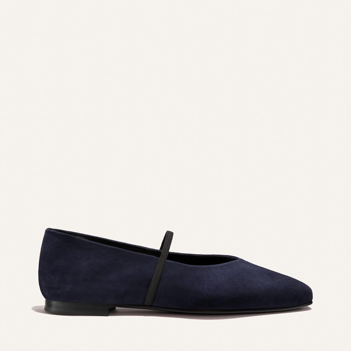 The Phoebe - Indigo Suede by Margaux is a ballet flat crafted from rich navy suede, featuring a thin black strap across the instep, a black sole, and a simple, minimalist silhouette. Made with sacchetto construction for exceptional comfort—the softest flat—it's shown in side profile against a plain light background.