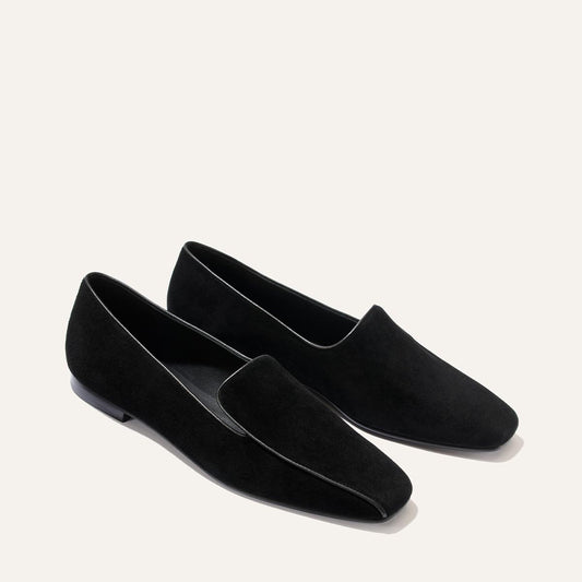 A pair of Margaux’s The Portia Loafer in black suede, featuring a minimalist design, are displayed on a light, neutral background.