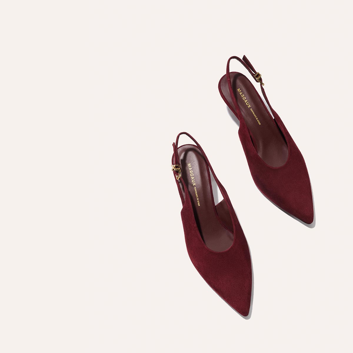 The Prado Sling - Burgundy Suede flats by margaux-development feature pointed toes and gold buckle details, shown on a light beige background.