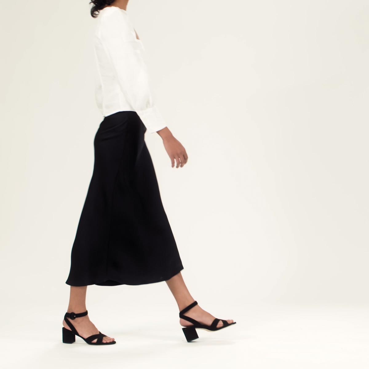 The City Sandal in Black Suede shown on model styled with a black midi skirt and a white long sleeve blouse with a square neck.