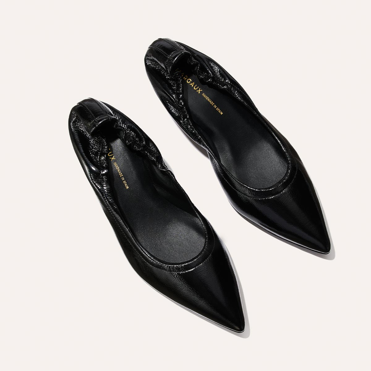 The Margaux Roma 40 – Black Crinkle Patent is a pair of pointed-toe ballet flats featuring gathered heel detailing, shown on a light background.