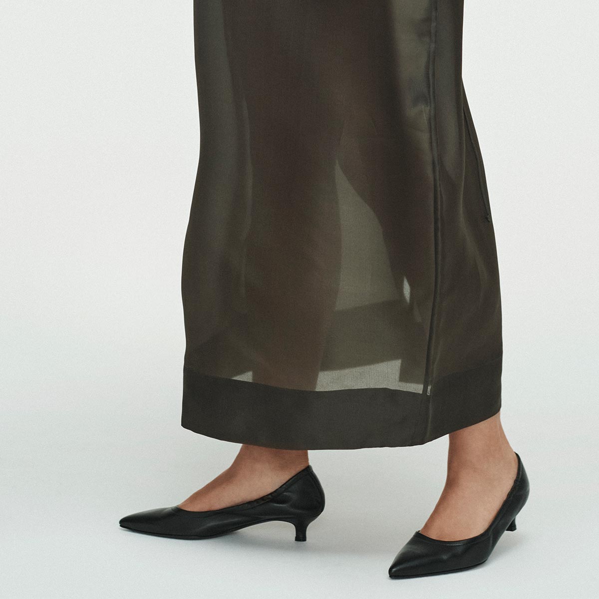 A person wearing a sheer black skirt and chic Margaux heels, The Roma 40 - Black Nappa, stands on a white background.