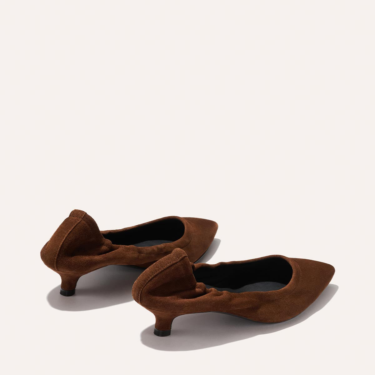 The Roma 40 - Ganache Suede by Margaux are brown suede pointed-toe flats with chic ruched detailing and a subtle heel, showcased against a plain light background.