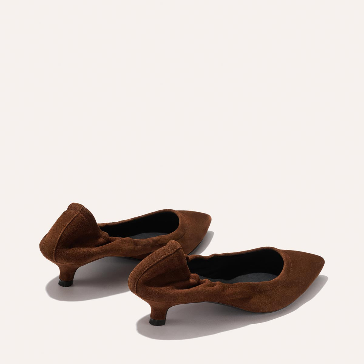 A pair of Margaux's The Roma 40 in Ganache Suede—women’s brown suede low-heeled shoes featuring pointed toes and ruched details—set against a plain light background, offering effortless style with a comfortable, walkable heel.