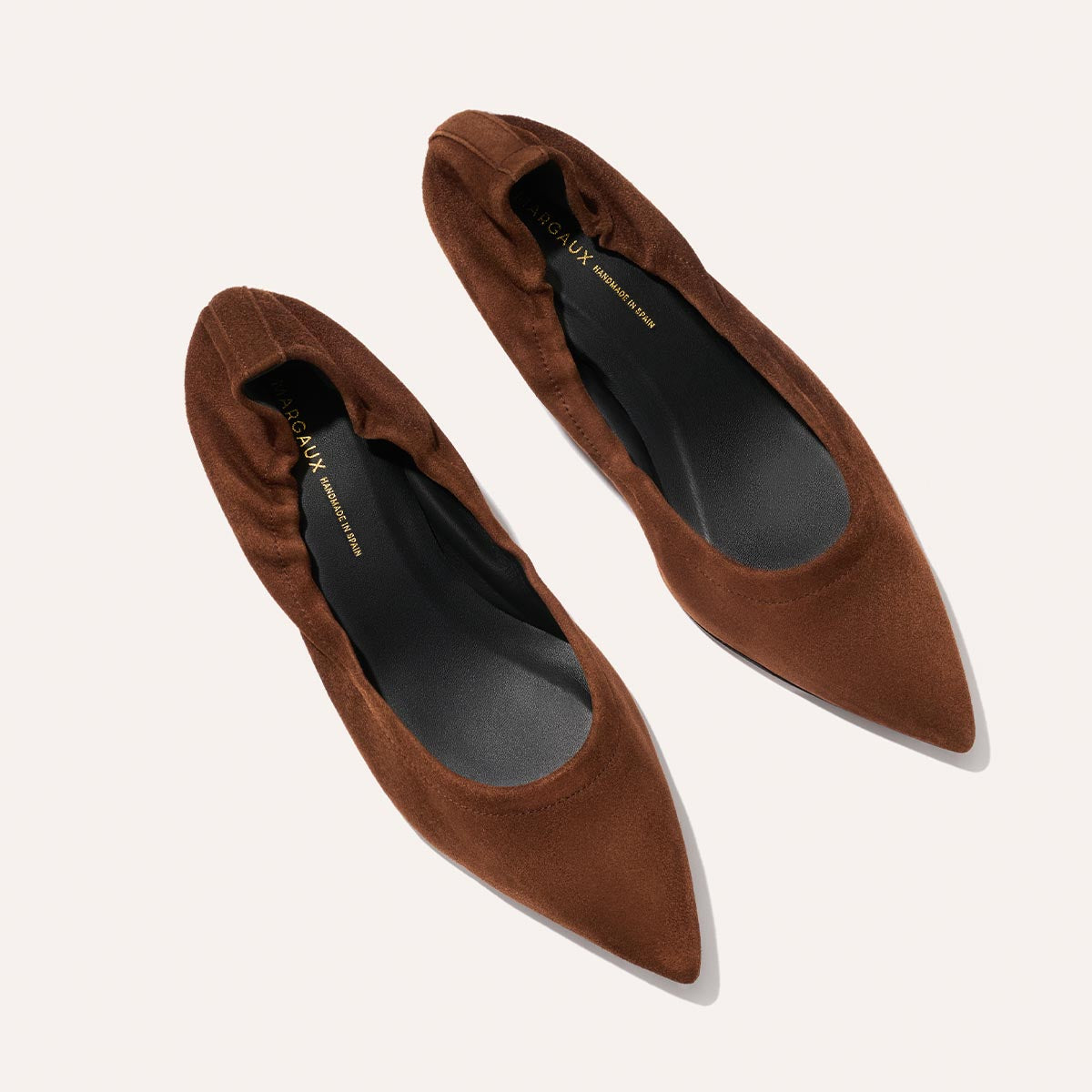 A pair of Margaux's The Roma 40 flats in Ganache Suede, featuring brown pointed toes, elasticized edges, and a comfortable heel, viewed from above on a light background.
