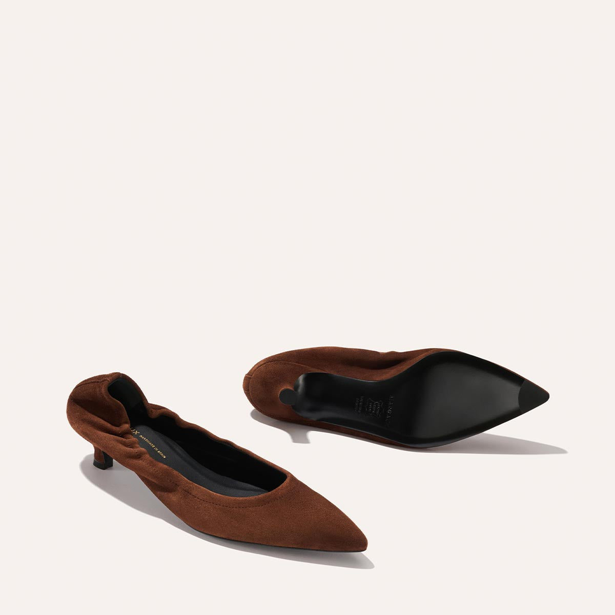A pair of Margaux’s The Roma 40 - Ganache Suede shoes—featuring a walkable kitten heel for all-day comfort—with one shoe upright and the other lying on its side, displayed against a plain light background.
