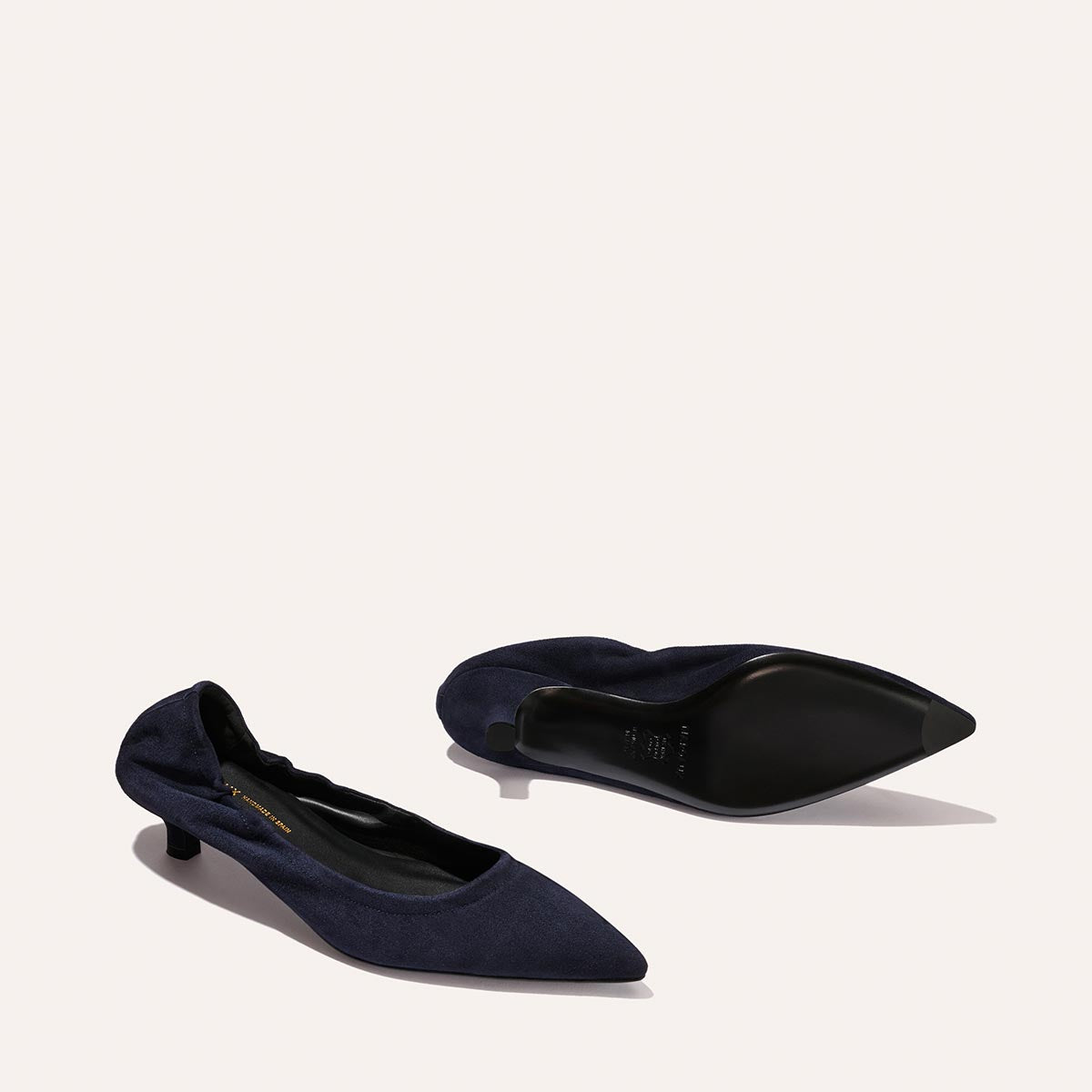 A pair of Margaux’s The Roma 40 in Indigo Suede—sleek pointed-toe heels with low, comfortable heels—one shoe upright and the other on its side, are elegantly displayed against a light background.