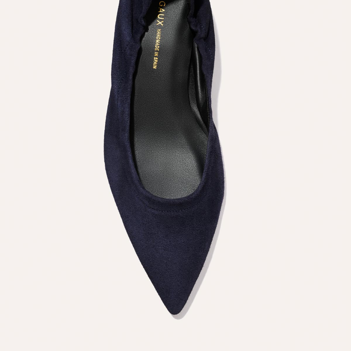 Close-up top view of The Roma 40 - Indigo Suede by Margaux, a dark blue pointed-toe flat with a black insole, shown against a light background.