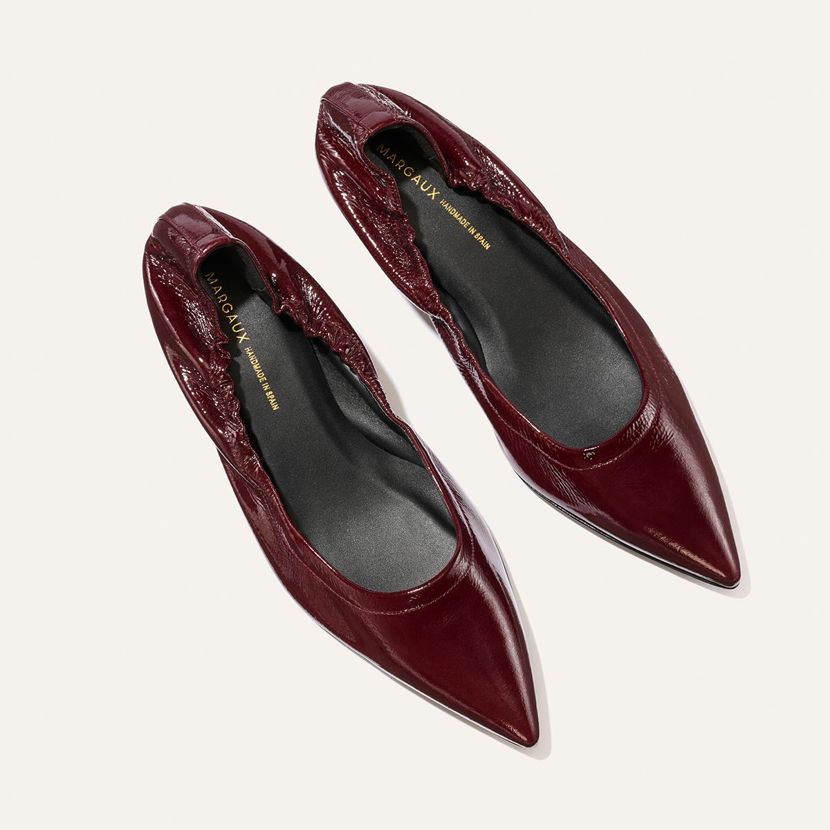 A pair of Margaux The Roma 40 - Merlot Crinkle Patent pointed-toe flats with elastic backs, photographed from above on a light background.