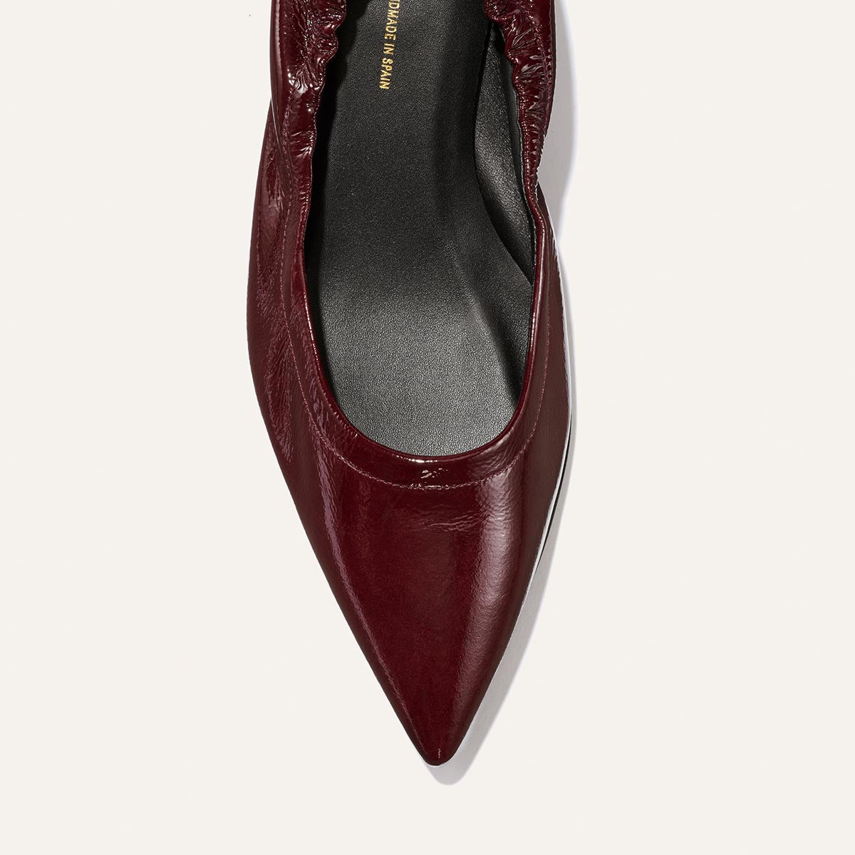 A top view of The Roma 40 - Merlot Crinkle Patent by Margaux, a pointed-toe flat in dark red crinkle patent leather with a gathered edge and black insole, is shown against a white background.