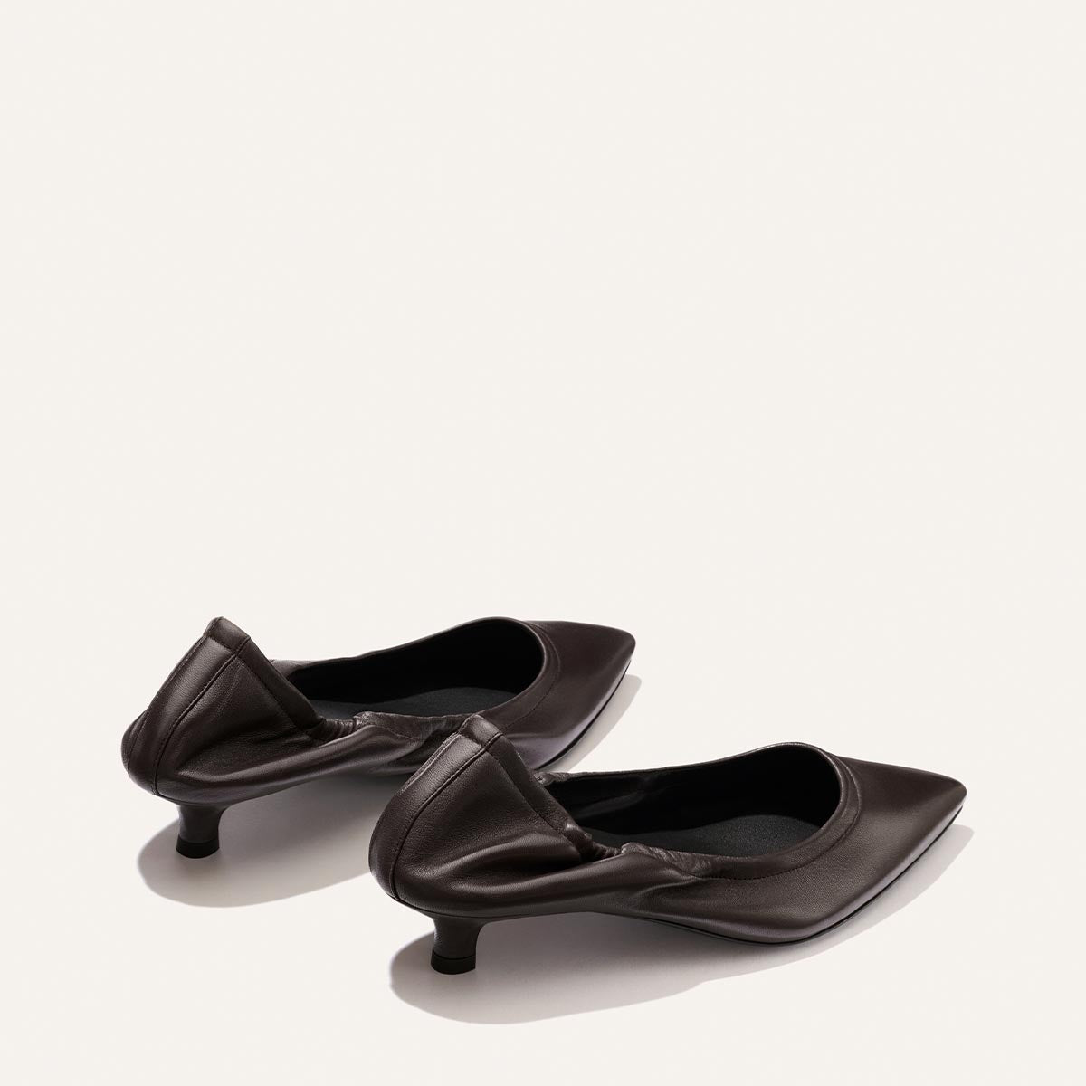 A pair of The Roma 40 - Espresso Nappa heels by Margaux, featuring a pointed toe, low thin kitten heel, and ruching detail at the back, epitomizes chic style against a plain light background.
