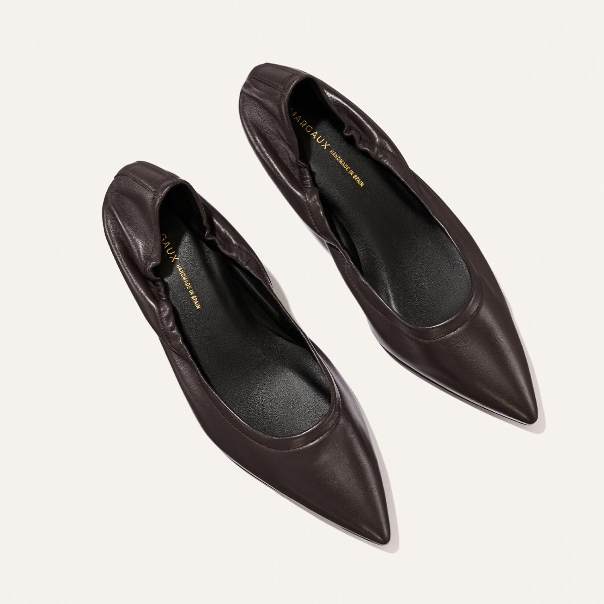 A pair of The Roma 40 - Espresso Nappa pointed-toe flats by Margaux, crafted in dark brown leather with gathered detailing at the heel, displayed on a light background for a timeless yet chic look.