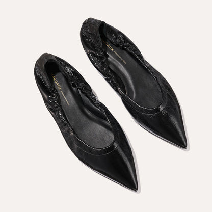 The Margaux The Roma - Black Crinkle Patent features black pointed-toe ballet flats with a gathered, elasticized heel and a smooth patent finish, displayed on a light background.