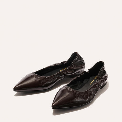 The Roma - Cocoa Crinkle Patent by Margaux are dark brown, pointed-toe ballet flats with a crinkled patent finish and ruched opening, shown on a light background.