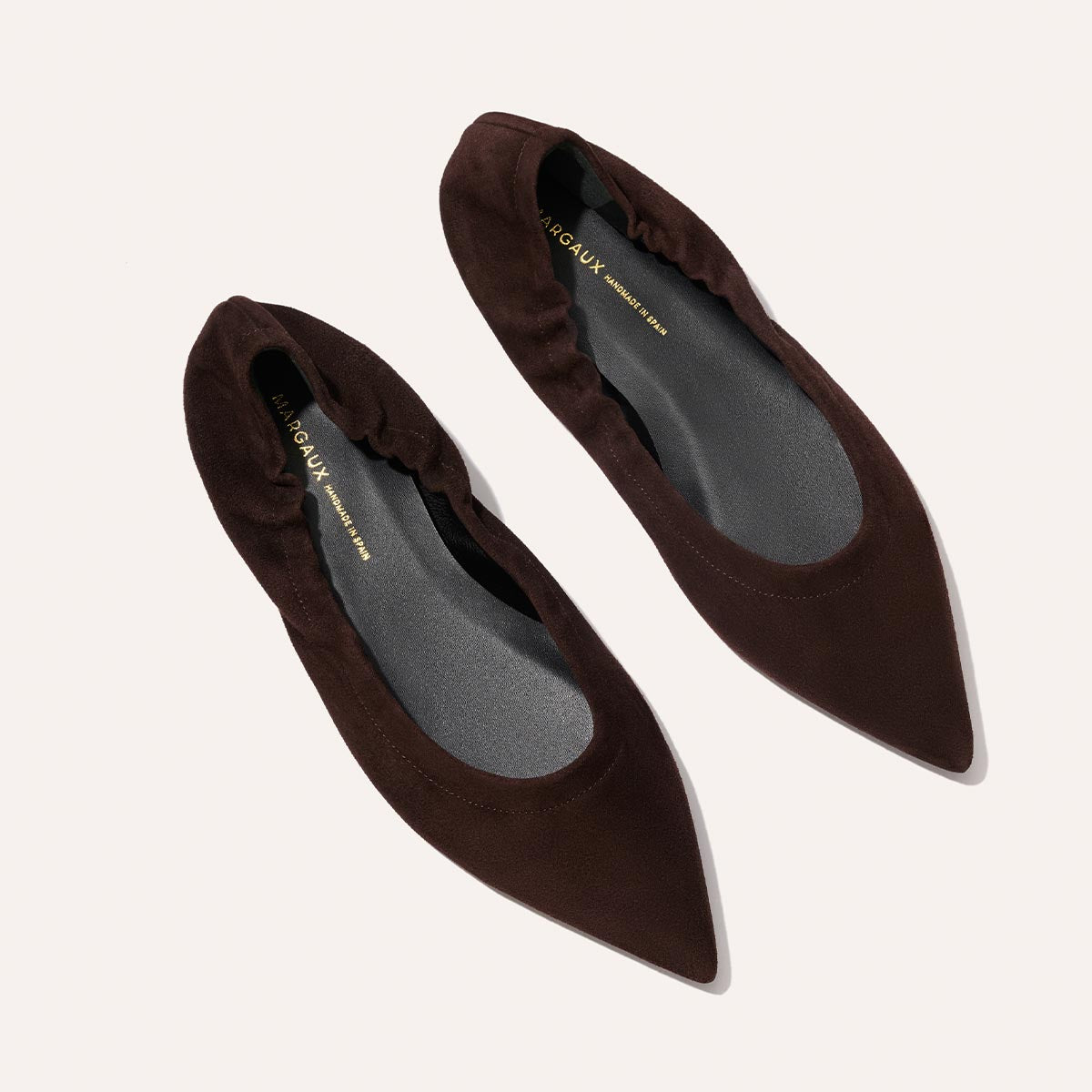 The Roma - Espresso Suede by Margaux: a pair of dark brown, pointed-toe flats with elasticized sides, shown on a light background.