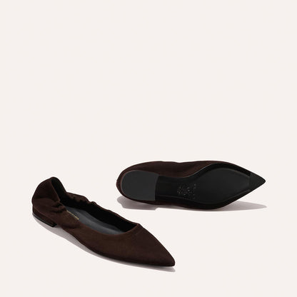 Two Margaux Roma flats in Espresso Suede—one on its side, the other showing a black sole—are displayed on a light, neutral background.