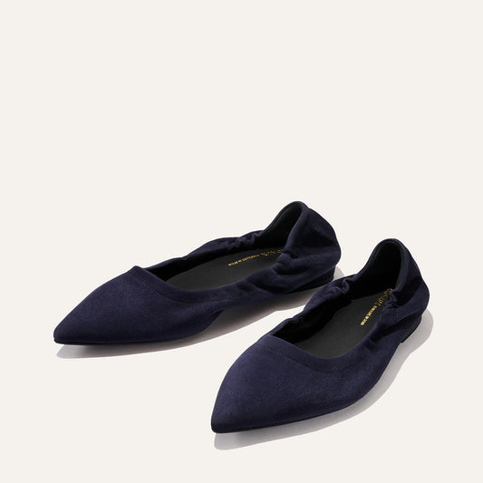 A pair of Margaux's The Roma - Indigo Suede pointed-toe ballet flats, featuring gathered detailing at the sides, is displayed on a light background.