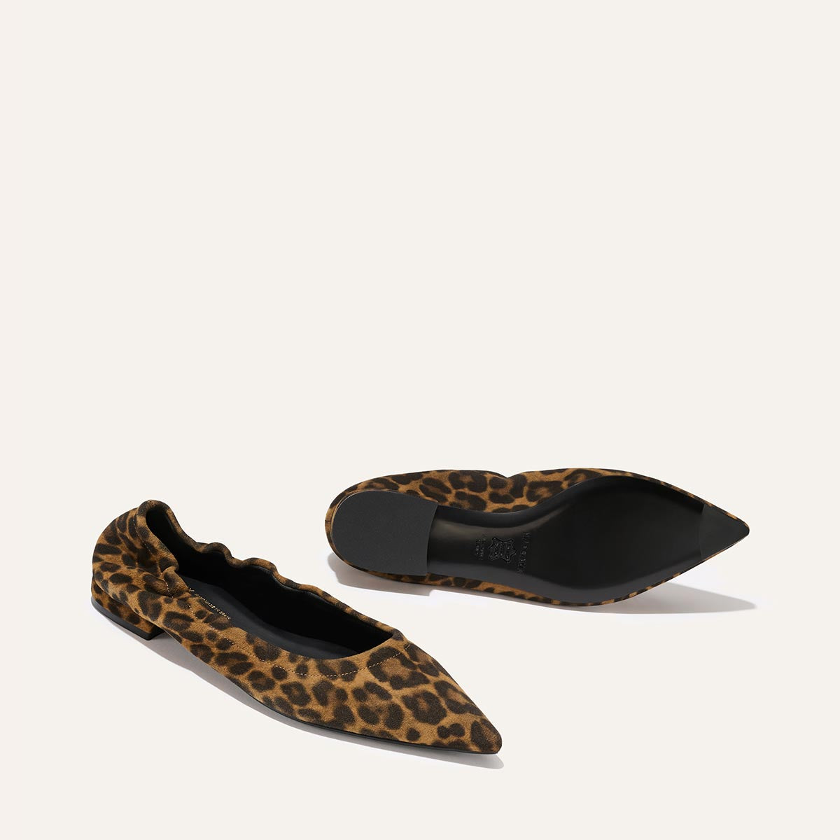 Margaux's The Roma - Leopard Suede ballet flats feature a pointed toe and brown and black leopard print; one shoe stands upright while the other rests on its side, both set against a plain light backdrop.