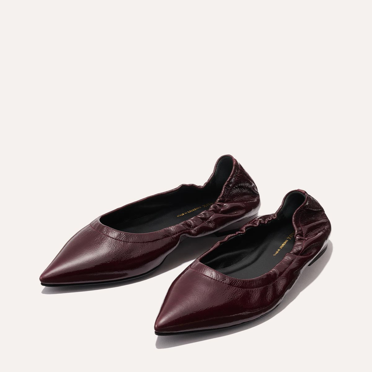 The Margaux Roma - Merlot Crinkle Patent is a sophisticated pointed-toe ballet flat in burgundy with a gathered, elasticized edge and glossy finish, displayed on a neutral background.