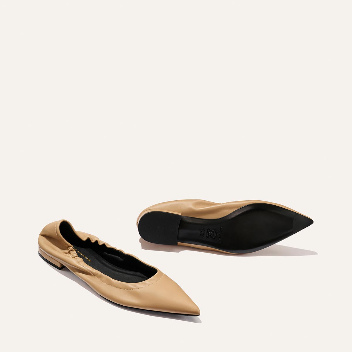 A pair of Margaux's The Roma - Praline Nappa flats, one showing the ruched tan upper and the other the sole, are displayed on a plain light background.