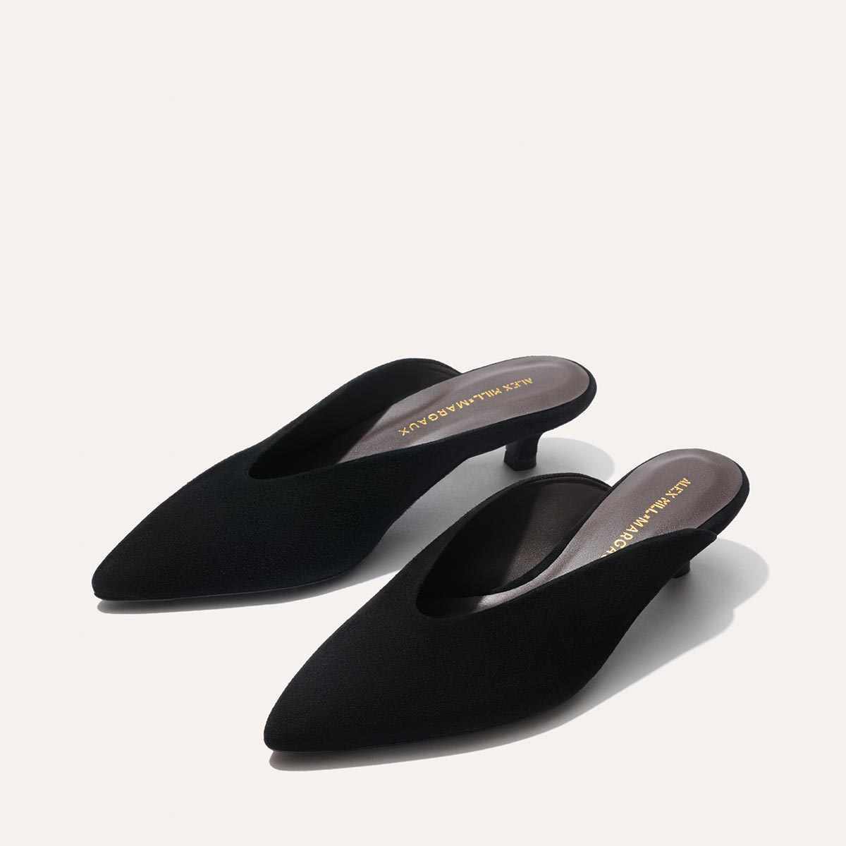 The Romy - Black Suede kitten mule heels by Margaux showcase "Alex Mill x Margaux" in gold on the insoles—a sleek party shoe with pointed toes, elegantly set against a plain light background.